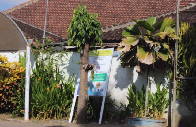 Foto : Posisi papan nama proyek bersandar ditembok pagar kecamatan cluring posisi tepatnya dibalik pohon. (Doc. Rony).